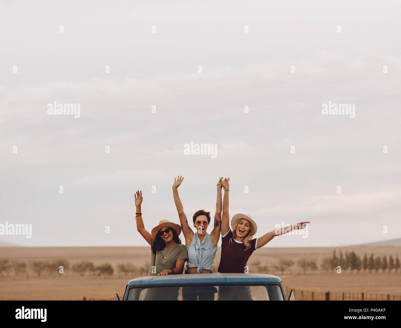 Gruppe von Freunden auf einem Roadtrip durch die Landschaft. Drei junge Frauen, der in der Rückseite eines offenen Lkw lachend mit der Hand angehoben. Stockfoto