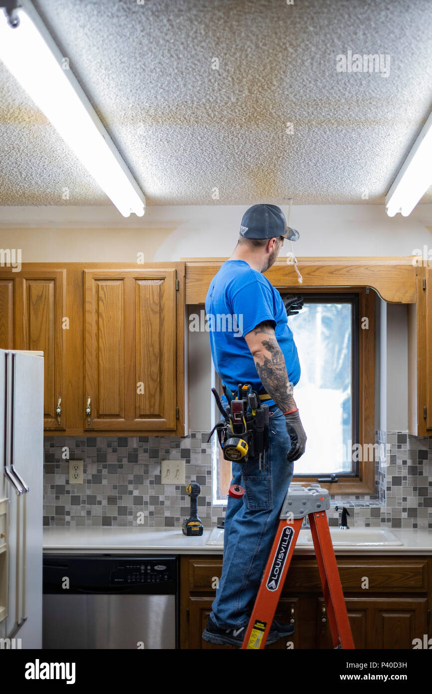 Kaukasische mann Elektriker stehen auf Leiter und ändern Sie leuchtet während einer Küche Renovieren in Wichita, Kansas, USA. Stockfoto