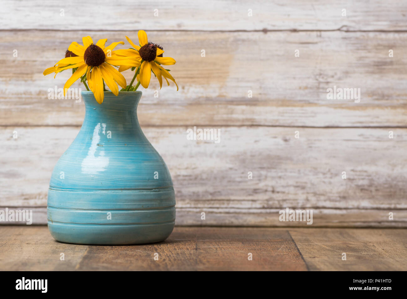 Black Eyed Susan Blumen in einem vintage Blue Keramik Vase und Holz- Hintergrund Stockfoto