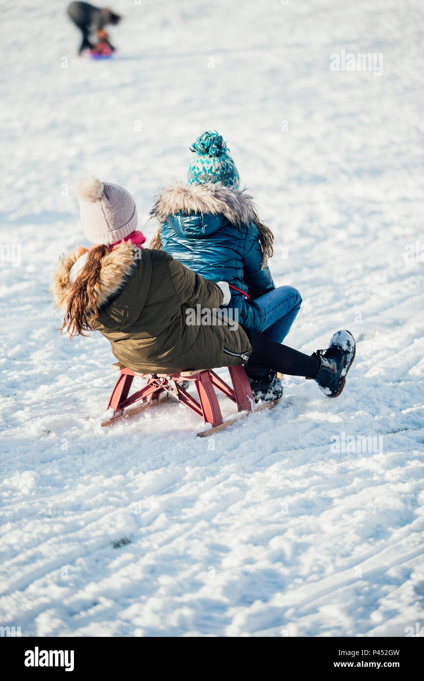Ansicht der Rückseite zwei Mädchen Schlittenfahren auf einem Hügel zusammen in den Schnee. Stockfoto