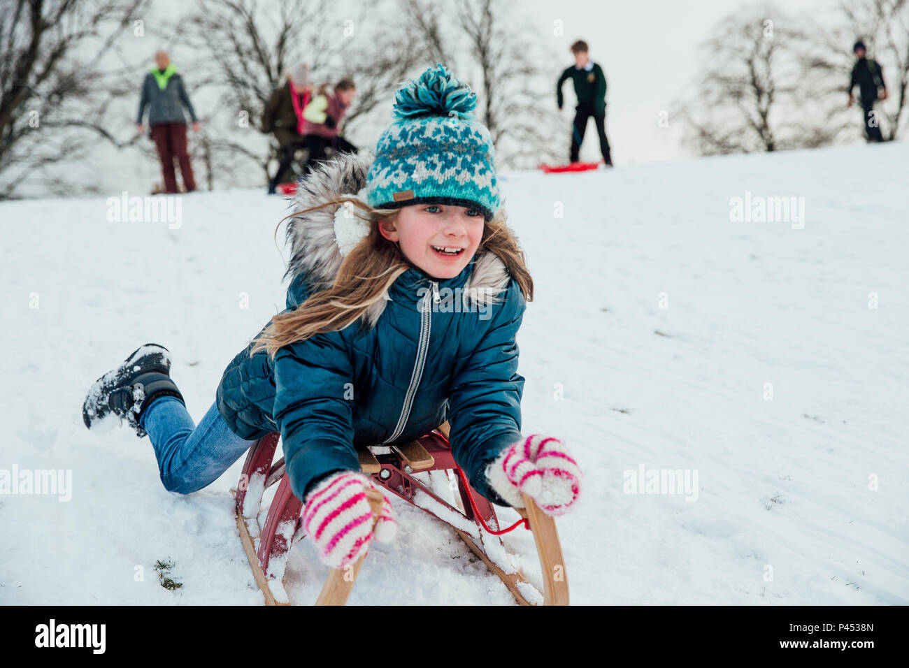 Kleines Mädchen liegt ihr der Bauch als Sie geht einen Hügel, der auf einem Schlitten im Schnee. Stockfoto