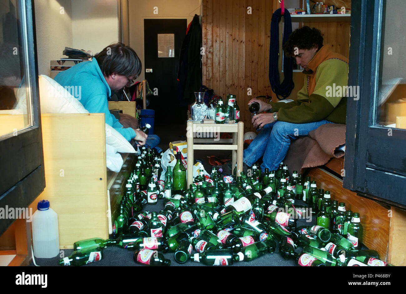 Eine ruhige Nacht in - zwei junge Männer Öffnen einer Bierflasche, umgeben von leeren Flaschen Stockfoto