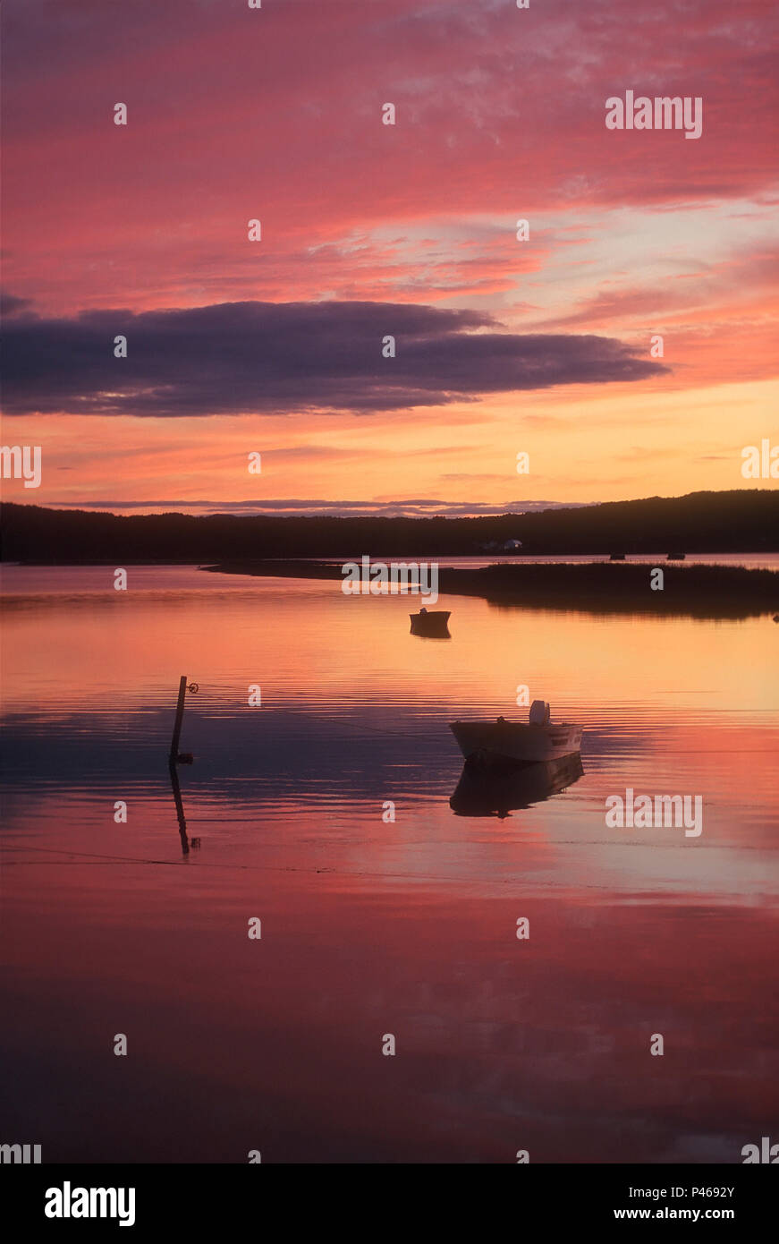 Ein dramatischer Sonnenuntergang auf ruhigem Wasser mit einem kleinen Boot wider Stockfoto