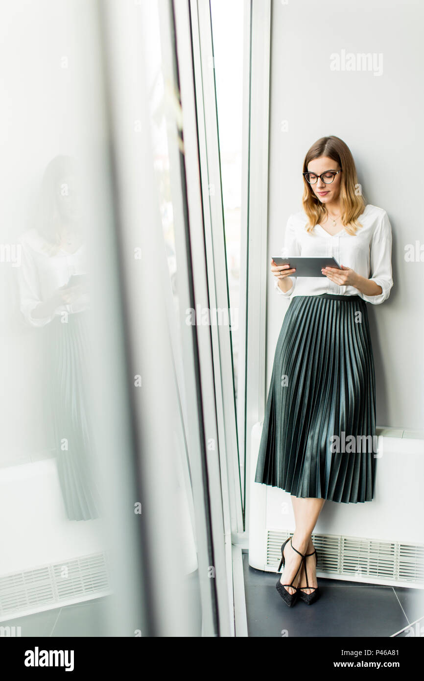 Junge attraktive weibliche Manager arbeiten an digitalen Tablet beim Stehen in modernen Büro Stockfoto