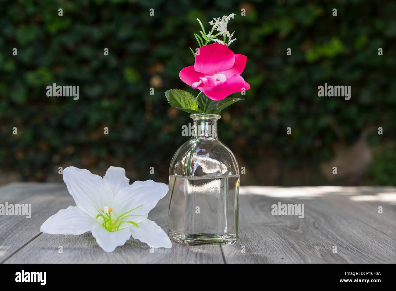 Eine Flasche und ein paar Blumen auf einem hölzernen Tisch im Freien im Sommer Stockfoto