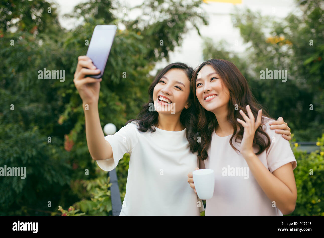 Lifestyle von zwei schönen Glück lange Haare Frauen sind mit Handy für Selfie im Garten. Asiatische weibliche Modelle Portrait Konzept. Stockfoto