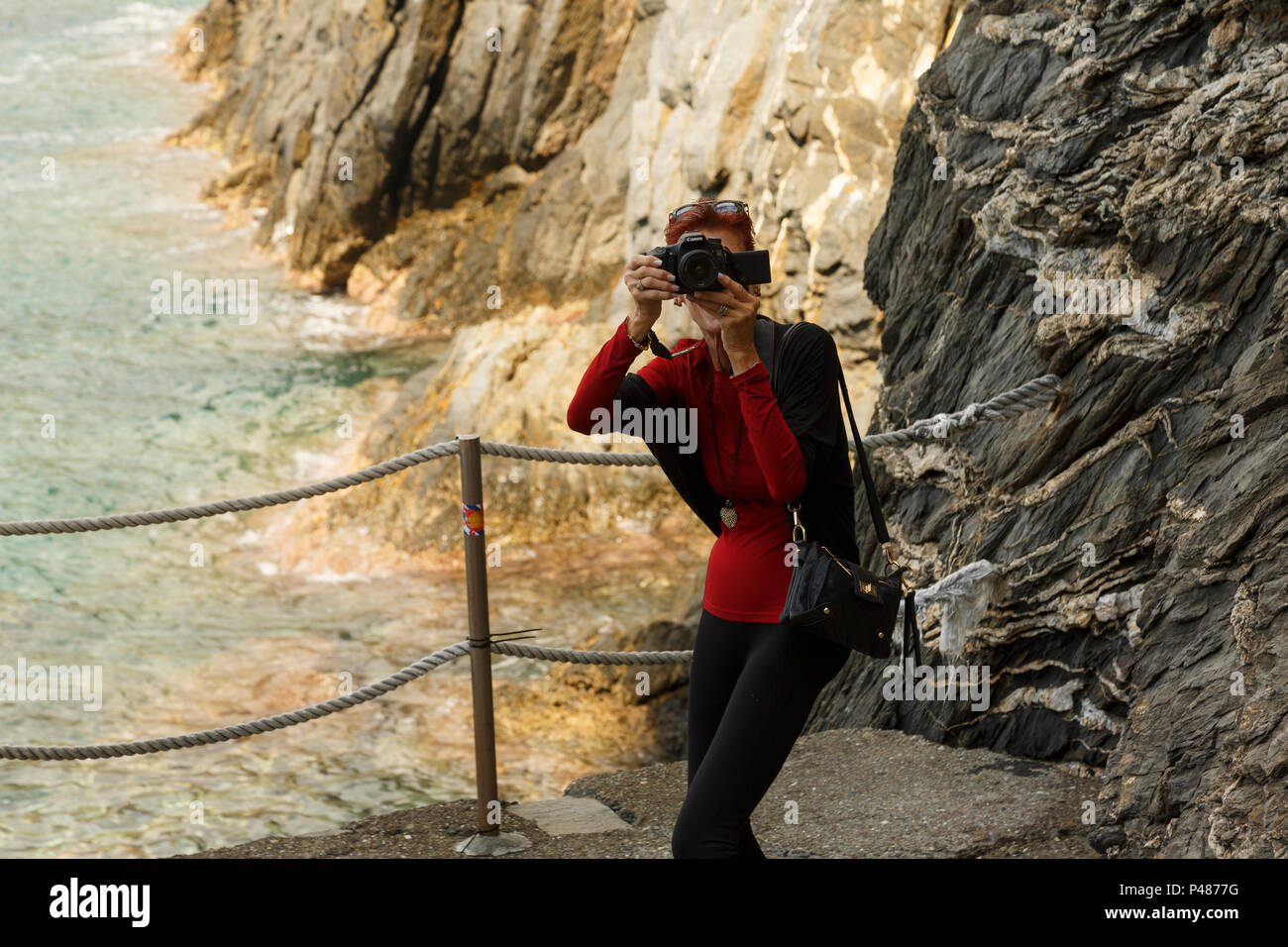 Solo Frau touristische Fotografen - videofilmer offen Schießen gegen Rocky seeküste Hintergrund, Manarola, Cinque Terre, Italien Stockfoto