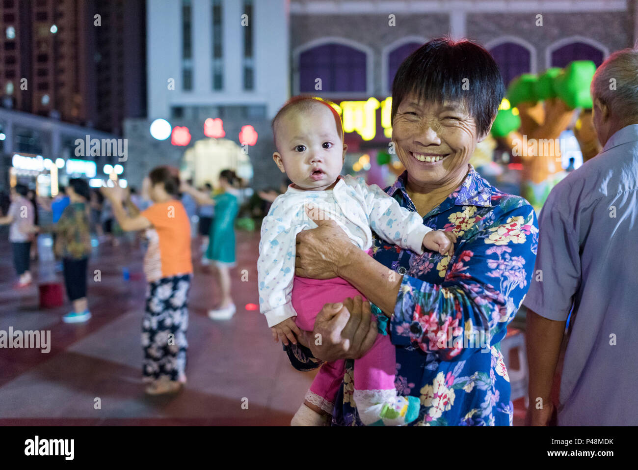 Großmutter kümmert sich um die Enkel inmitten Nachtleben in Central City Square, Libo, Provinz Guizhou, China. Stockfoto