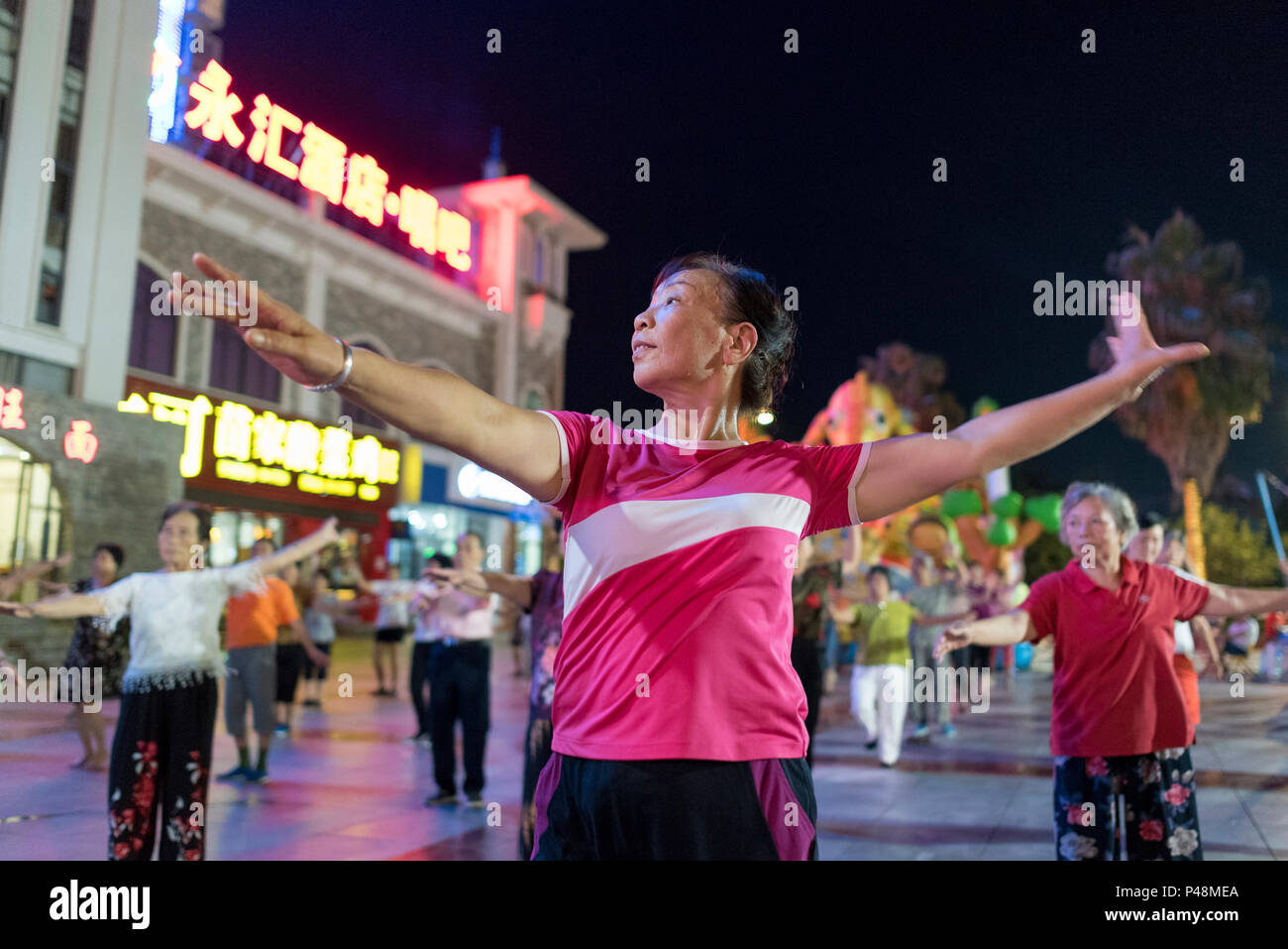 Reife Frauen Tanz und Bewegung zu Musik inmitten Nachtleben in Central City Square, Libo, Provinz Guizhou, China. Stockfoto