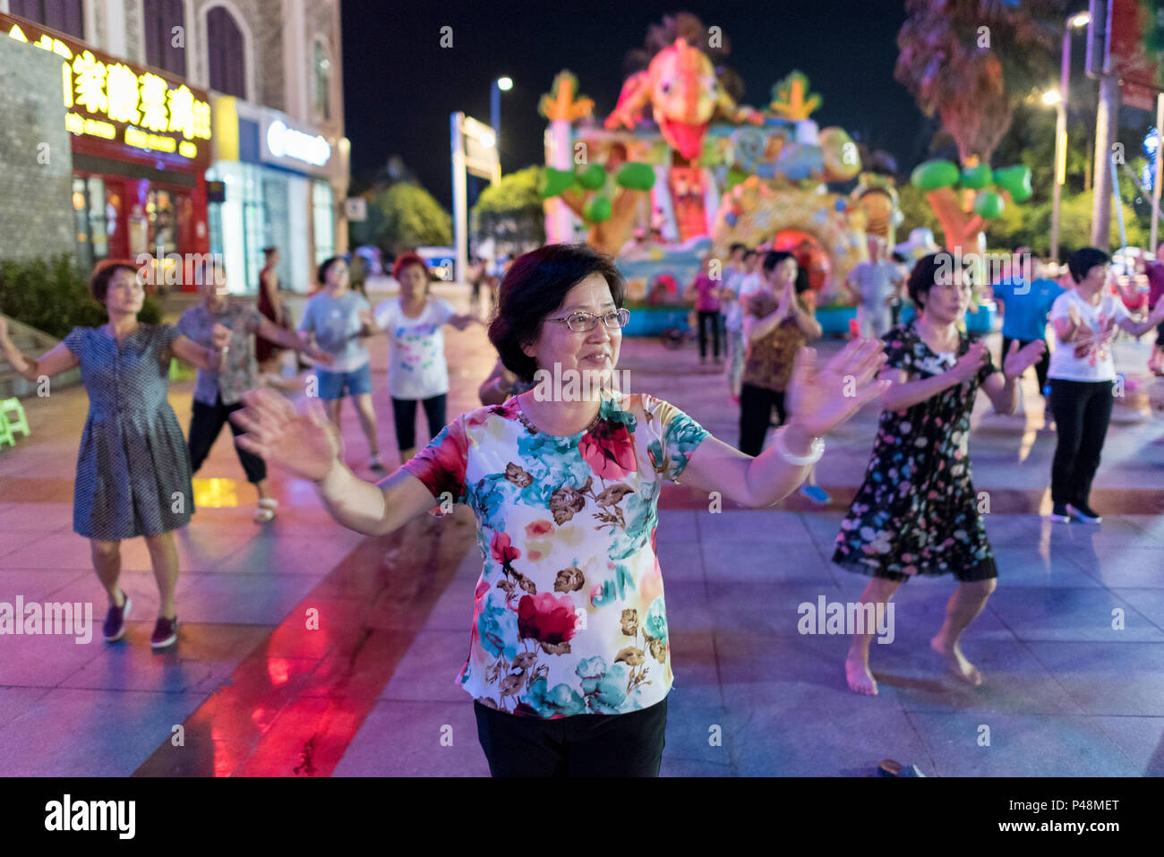 Reife Frauen Tanz und Bewegung zu Musik inmitten Nachtleben in Central City Square, Libo, Provinz Guizhou, China. Stockfoto