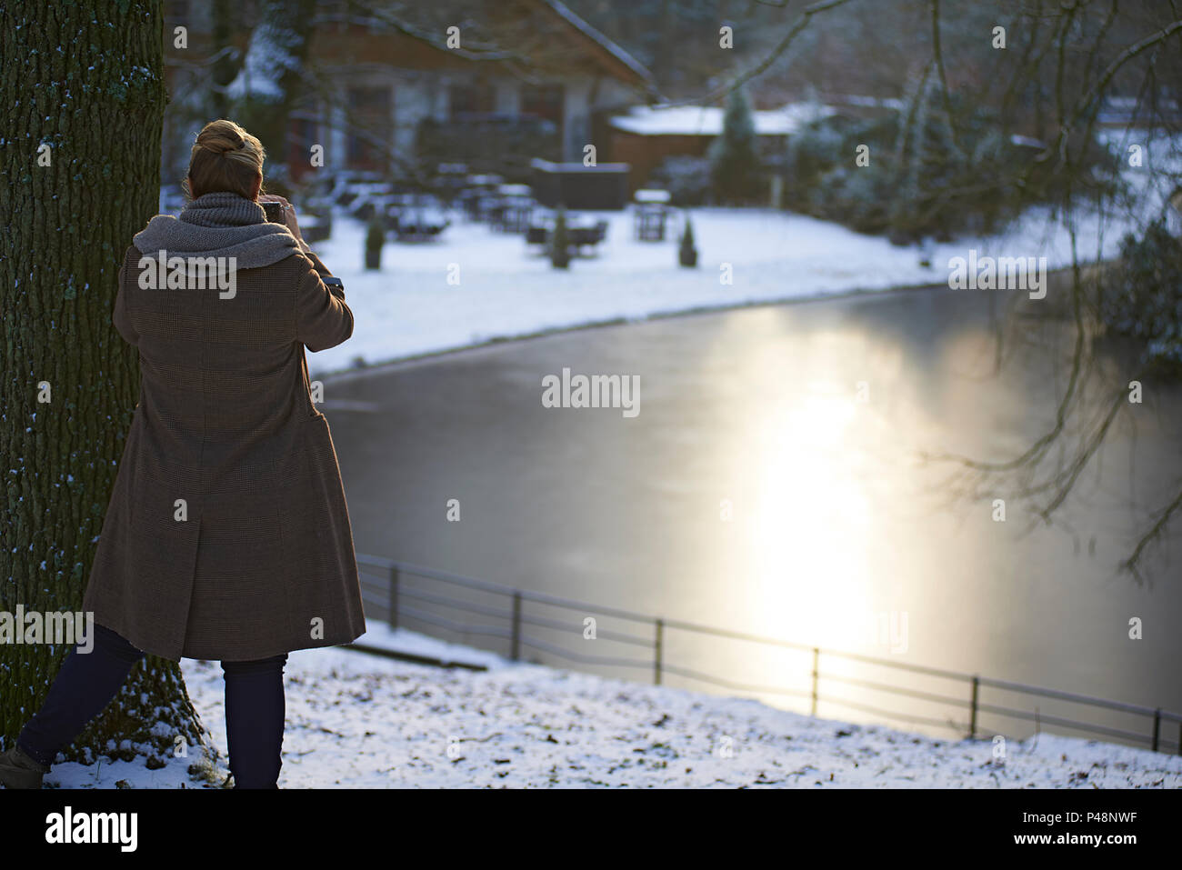 Über die Schulter geschossen von einer Frau Fotografieren von einem zugefrorenen See im Winter Sonnenschein Stockfoto
