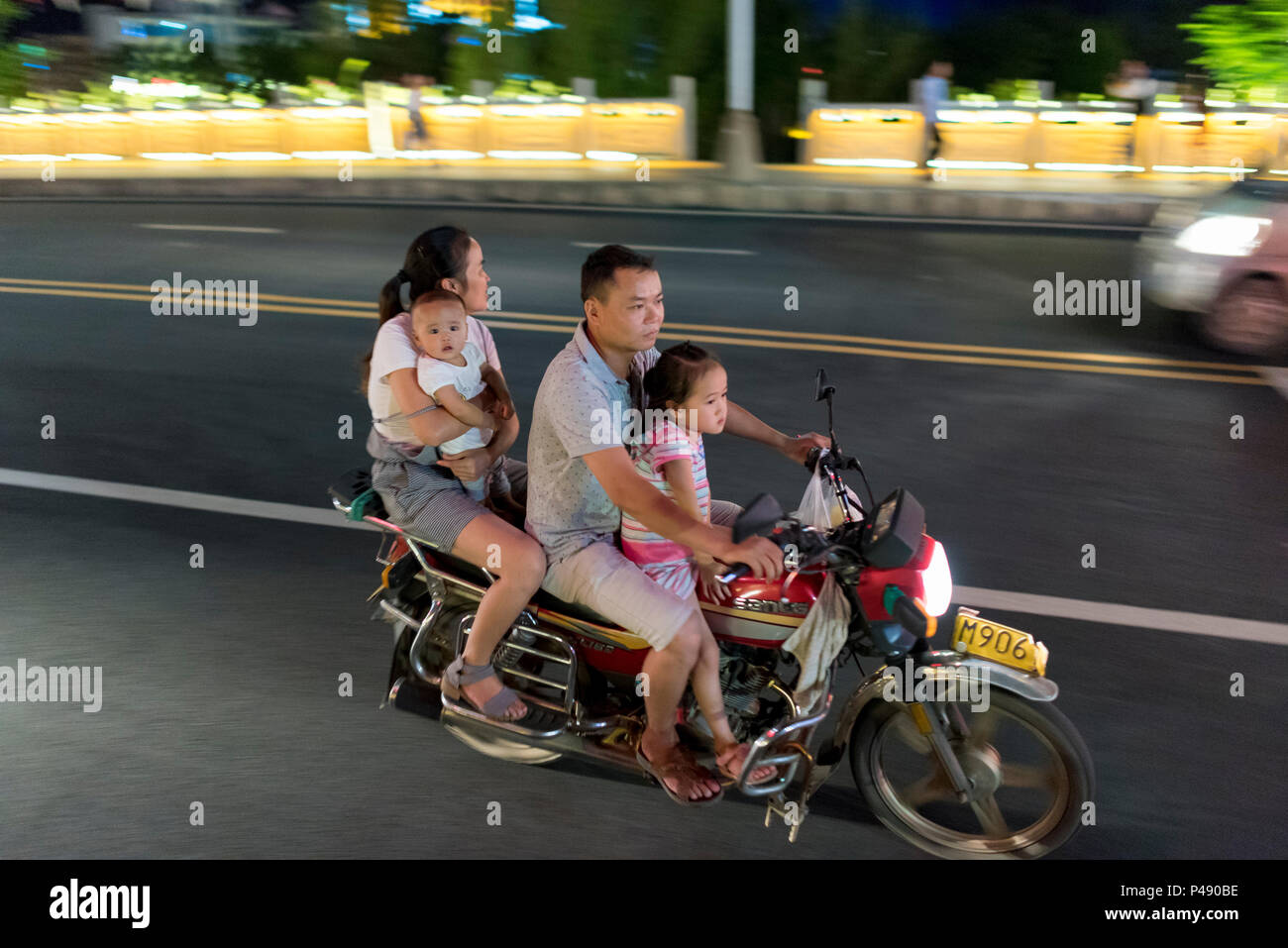 Familie der Mutter, Baby, Vater und Schwester auf Motorroller Geschwindigkeit durch die Innenstadt auf heiße Sommernacht, Libo, Provinz Guizhou Stockfoto