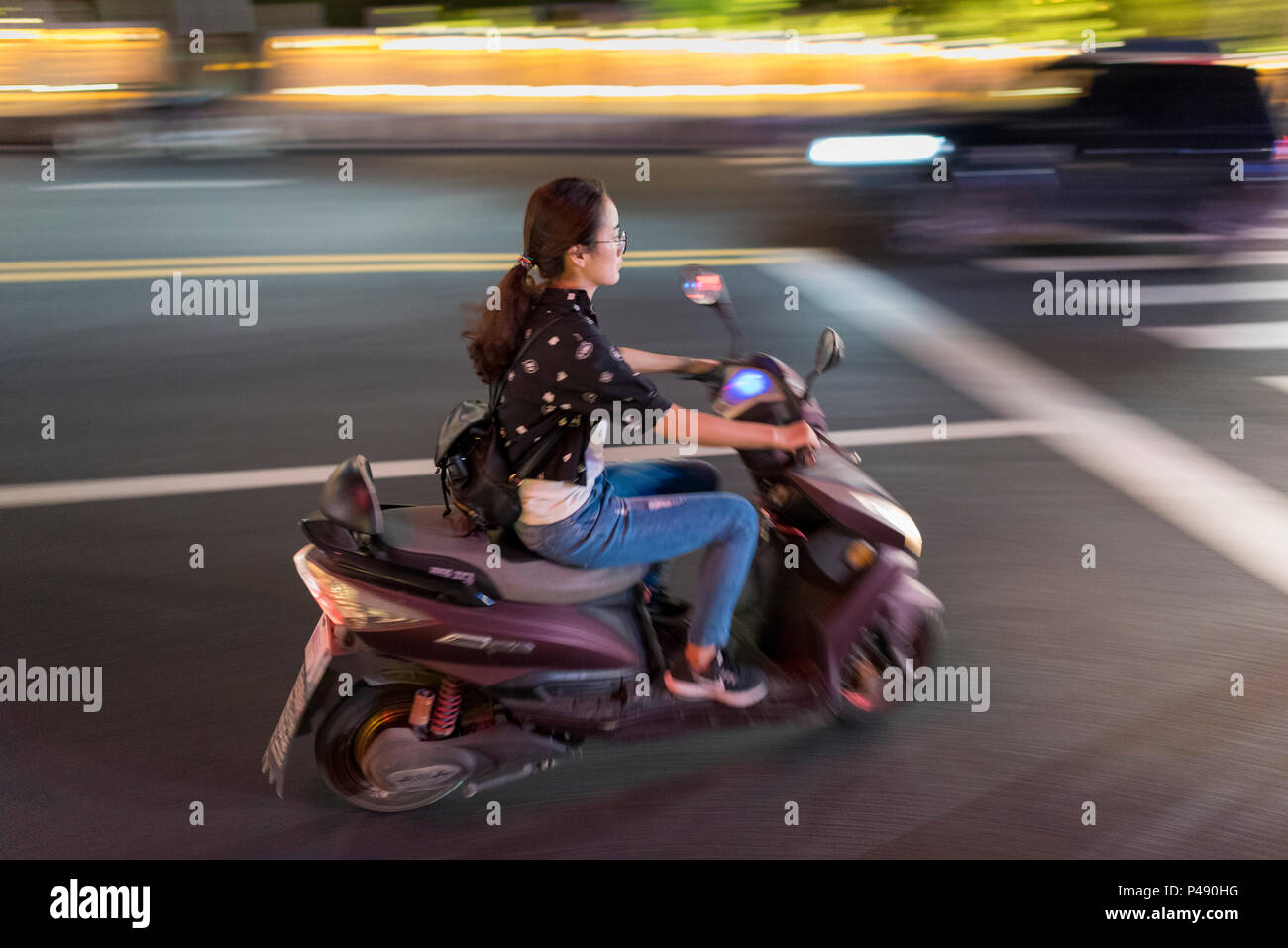 Junge Frau auf Motorroller Geschwindigkeiten durch Stadtzentrum auf heiße Sommernacht, Libo, Provinz Guizhou, China. Stockfoto