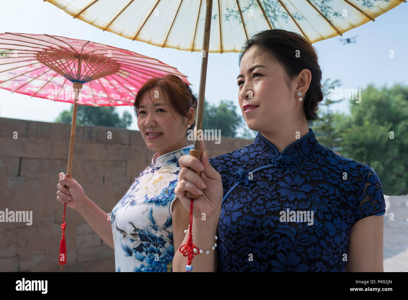 Reife Frauen in traditionellen eng anliegende Kleider tragen Papier Sonnenschirme Besucher begrüßen, Dong E E Jiao Stadt Liaocheng, Provinz Shandong, China Stockfoto