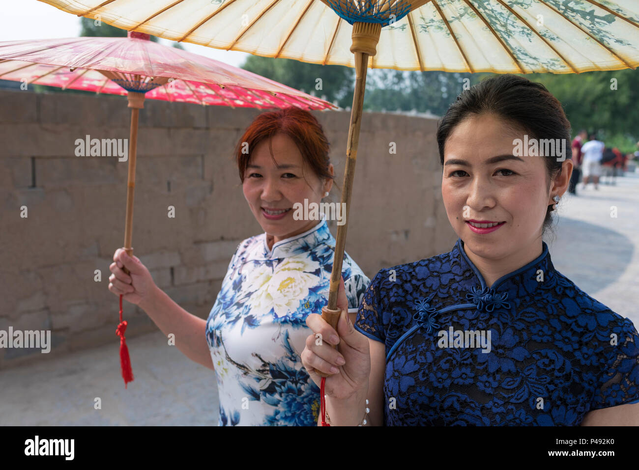 Zwei reife Frauen Akteure in traditionellen eng anliegende Kleider tragen Papier Sonnenschirme Besucher begrüßen, Dong E E Jiao Stadt Liaocheng, Stockfoto