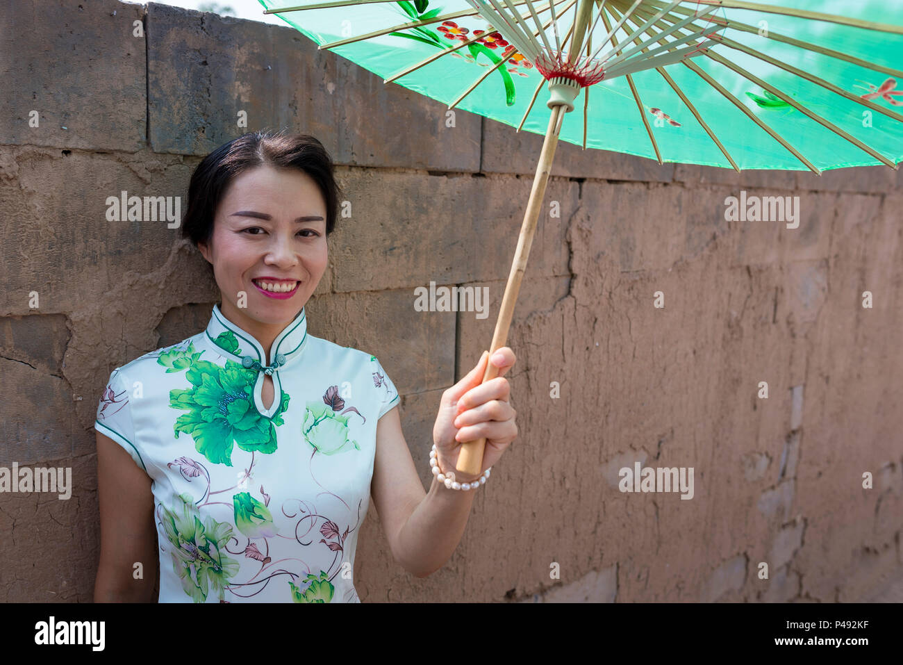 Reife Frau in traditionellen eng anliegende Kleider tragen Papier Sonnenschirm Besucher begrüßen, Dong E E Jiao Stadt Liaocheng, Provinz Shandong, China Stockfoto