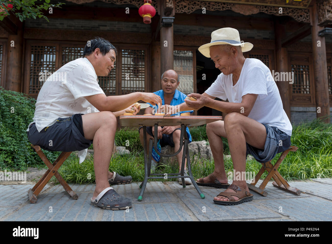 Drei Männer mit Freunden spielen Chinese Checkers in der Straße am Ende der heißen Sommertag, Nanyang Stadt, Qingzhou, Provinz Shandong, China Stockfoto