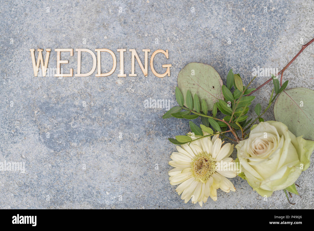Champagnerfarbenen Rosenblüte und beige Gerbera Blume liegen auf Beton. Das Wort Hochzeit war in Holz- buchstaben gelegt. Hintergrund mit viel Co Stockfoto