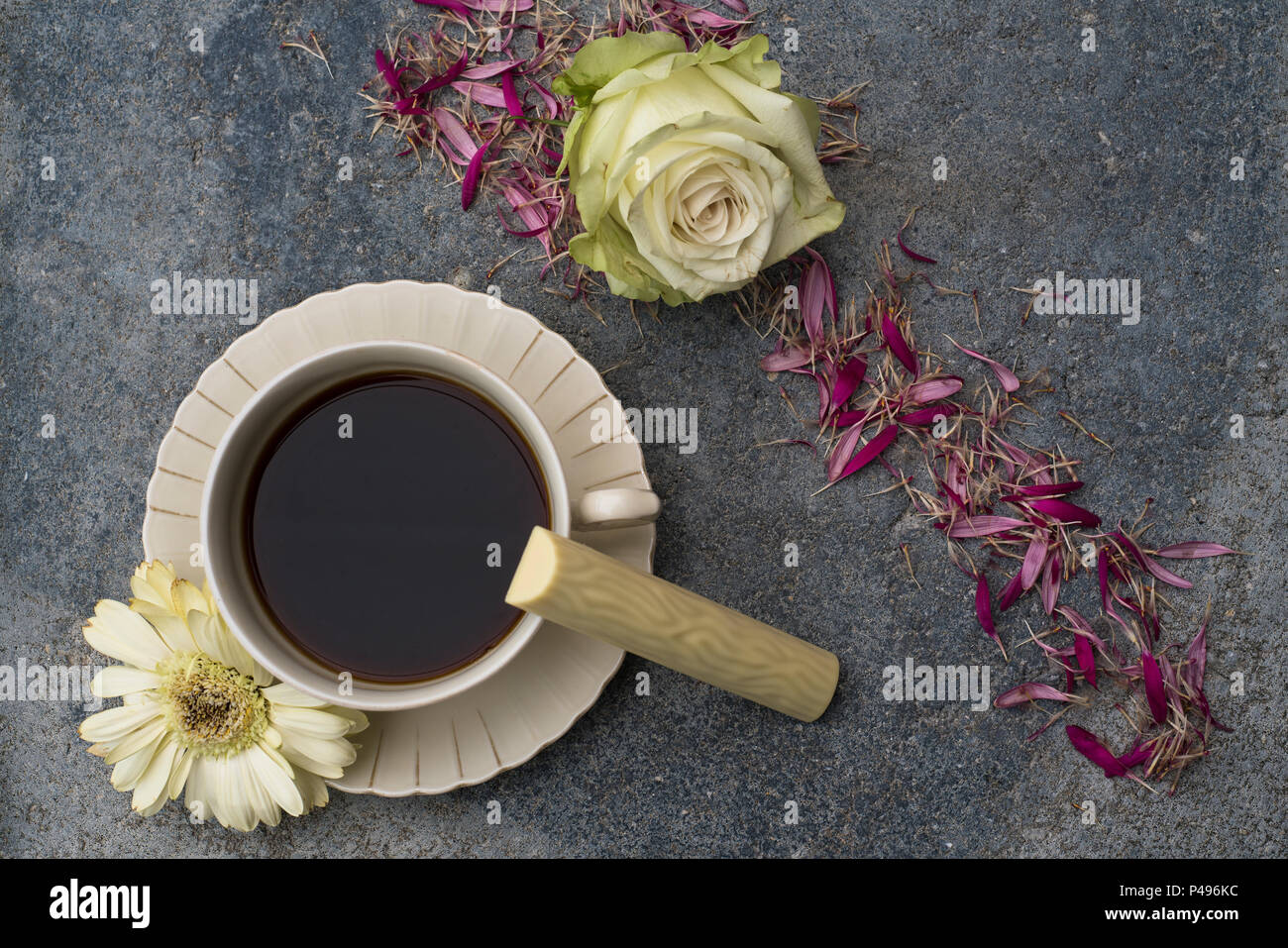 Eine Tasse mit Kaffee steht vor der dunklen konkreten Hintergrund. Champagnerfarbenen Blüten und Blumen Blüten das Bild schmücken. Eine Süßigkeit aus weißem Stockfoto