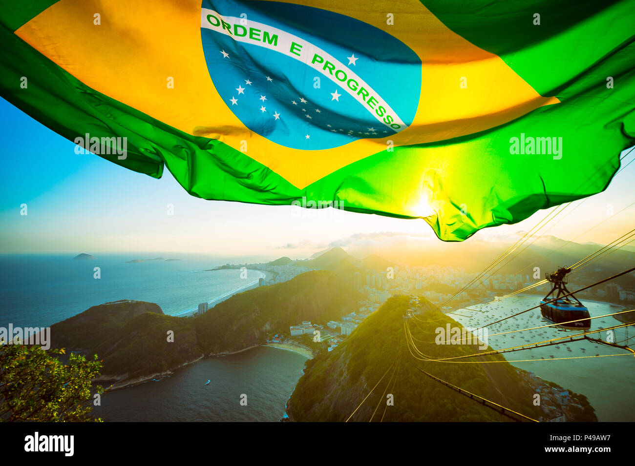 Brasilianische Flagge erstrahlt über dem goldenen Sonnenuntergang Skyline der Stadt am Zuckerhut in Rio de Janeiro. Stockfoto