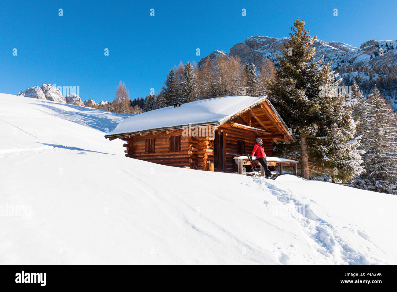 Ein Wanderer ist entspannend auf dem Schnee vor einer Berghütte in Gröden, Provinz Bozen, Südtirol, Trentino Alto Adige, Italien Stockfoto