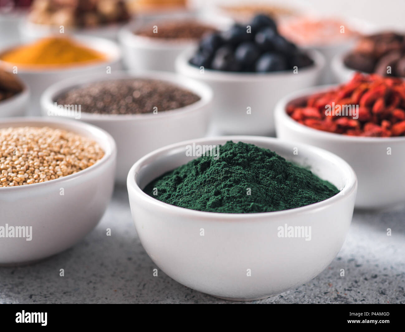 Spirulina Pulver in kleinen weißen Schale und andere superfoods für den Hintergrund. Selektive konzentrieren. Verschiedene superfoods Zutaten. Konzept und Grafik für superfood und entgiftende Lebensmittel Stockfoto