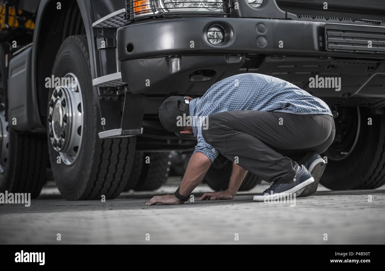 Problem mit Defekten Lkw, kaukasische Trucker in seinem 30s für Schäden unter seinem Fahrzeug suchen. Automobil- und Transportindustrie Thema. Stockfoto