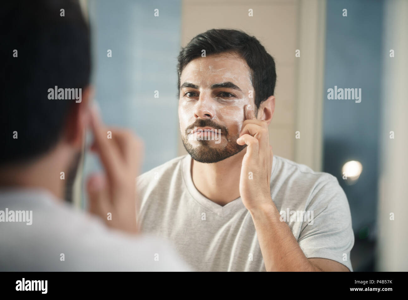 Junge hispanic Menschen und männlichen Schönheit. Metrosexuellen mann Anwendung Lotion für die Anti-Aging-Behandlung um Auge Stockfoto