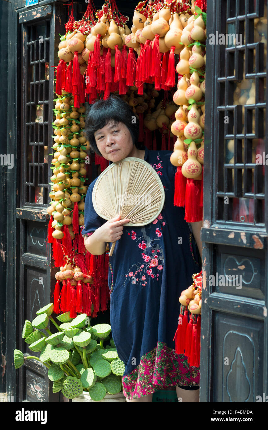 Frau Ladenbesitzer mit Ventilator im dekoriert Tür Kunden erwartet, Zhoucun touristischen Bereich, ZiboZibo, Shandong Province, China Stockfoto