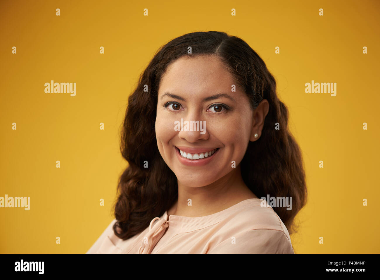 Fröhlich lächelnd hispanische Mädchen mit dunklen Haaren auf gelbem Hintergrund Stockfoto