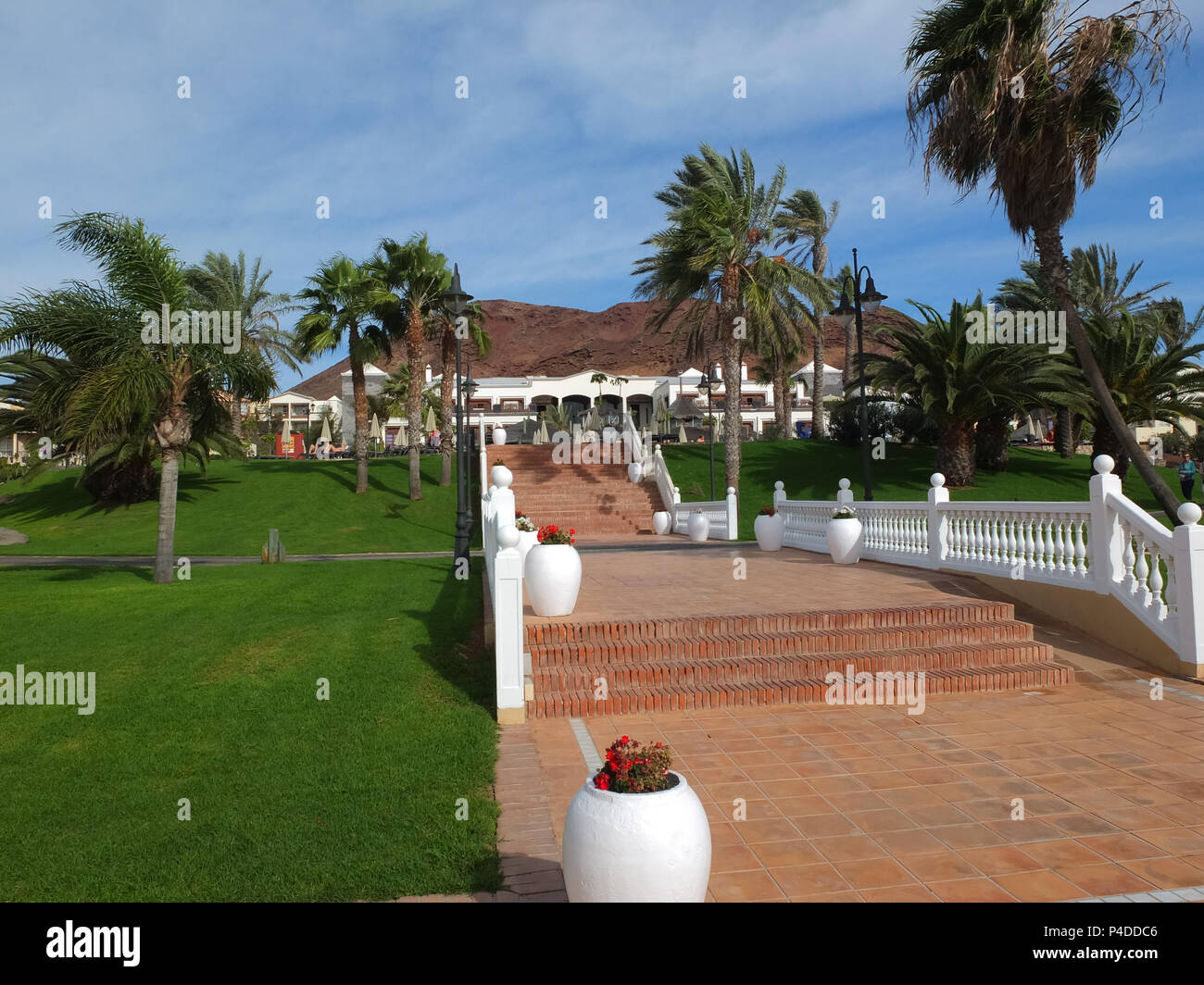 Lanzarote, Spanien - Dezember 09,2013: Lanzarote Palmen, rote Teracotta Treppen zum Hotel und vulkanische Berge hinter über lucious grünen Rasen im Dez Stockfoto