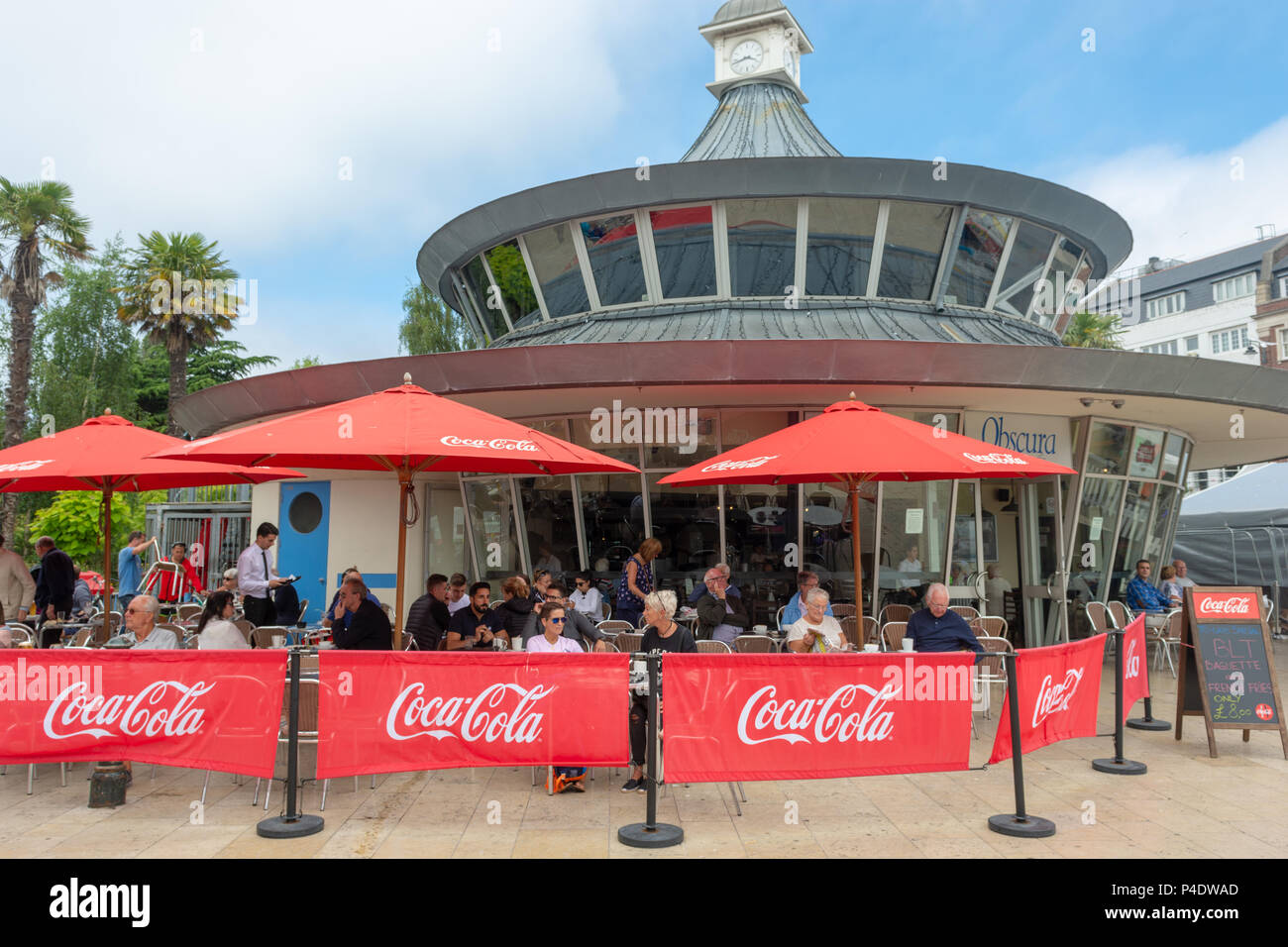 Menschen, die draußen hinter Coca-Cola-Bildschirmen im Cafe Obscura in The Square, Bournemouth, Dorset, Großbritannien, sitzen Stockfoto