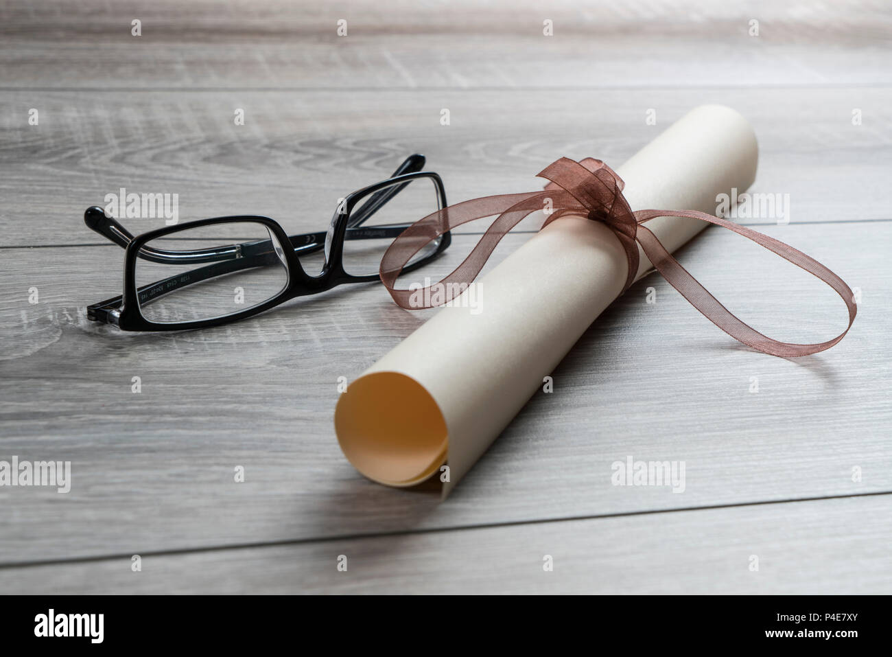 Ein Diplom aufgerollt und mit einem roten Band auf dem Tisch mit einer Brille gebunden Stockfoto