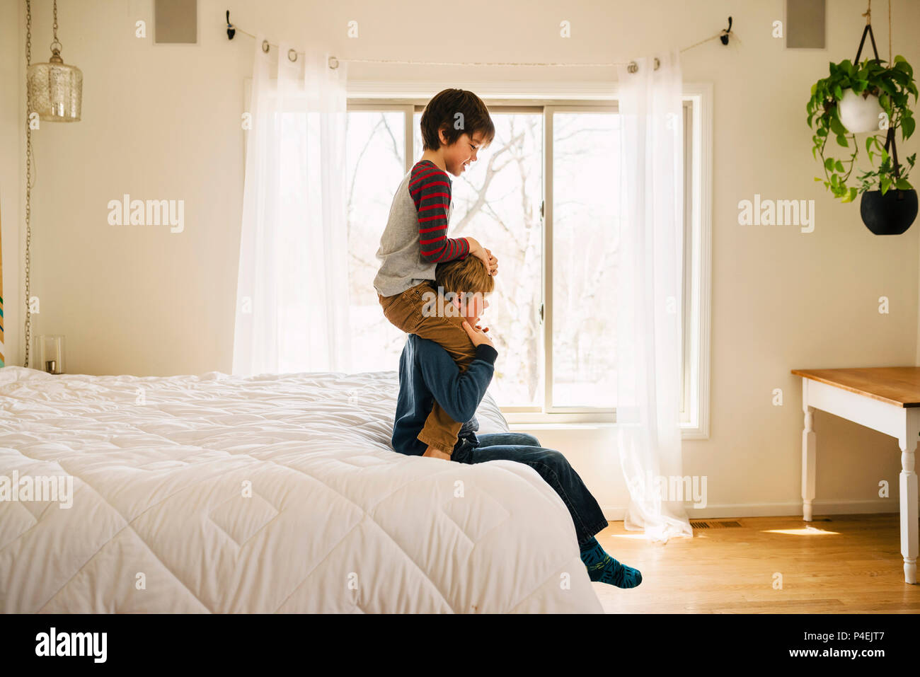 Junge sitzt auf einem Bett mit seinem Bruder auf den Schultern Stockfoto