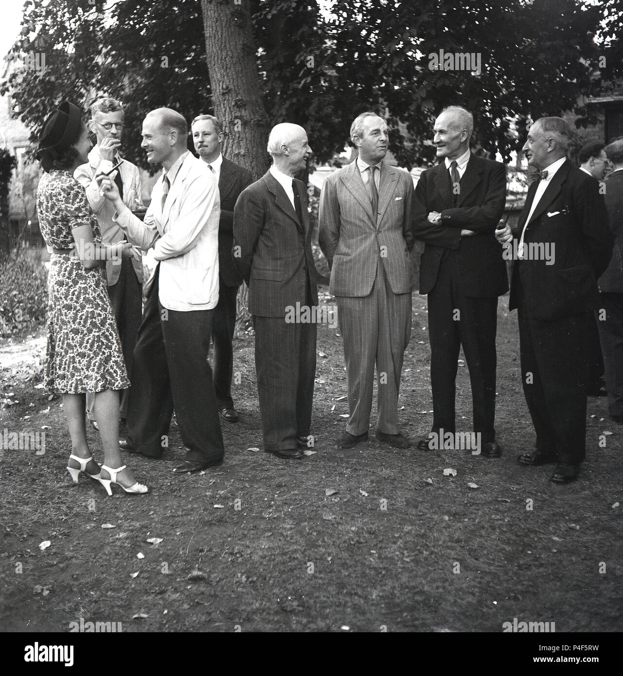 1948, historisch. Gut gekleidete ältere Herren und eine Dame draußen auf einer Gartenparty im Nachkriegs-England. Zwei der Herren rauchen Pfeifen, wie sie zu dieser Zeit bei Männern einer bestimmten Generation üblich sind. Stockfoto