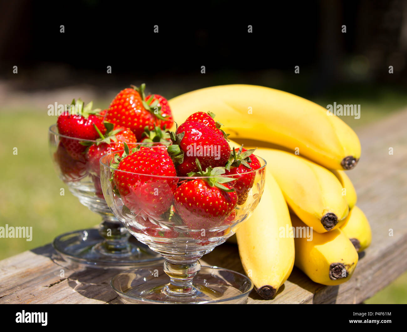 Nahaufnahme von frischen Erdbeeren in Glas Dessertspeisen & Bündel Bananen im Freien, sonnigen Sommertag. Genießen Sie UK Sommerferien im Garten. Staycation. Stockfoto