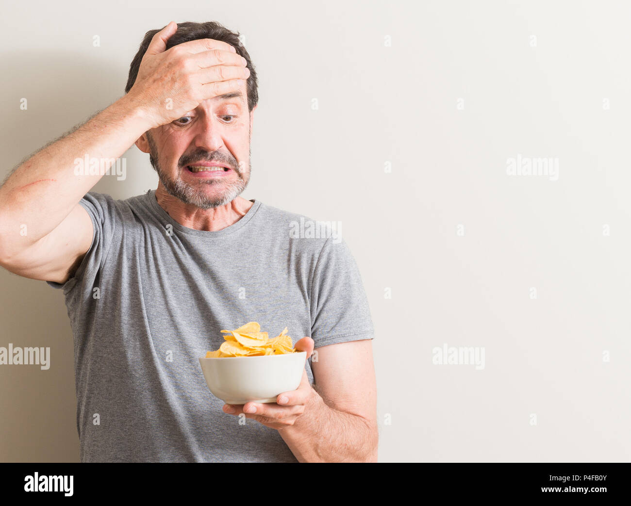 Älteren Menschen essen Kartoffelchips betonte, mit der Hand auf den Kopf, mit Scham und Überraschung Gesicht schockiert, wütend und frustriert. Angst und für Fehler stören. Stockfoto