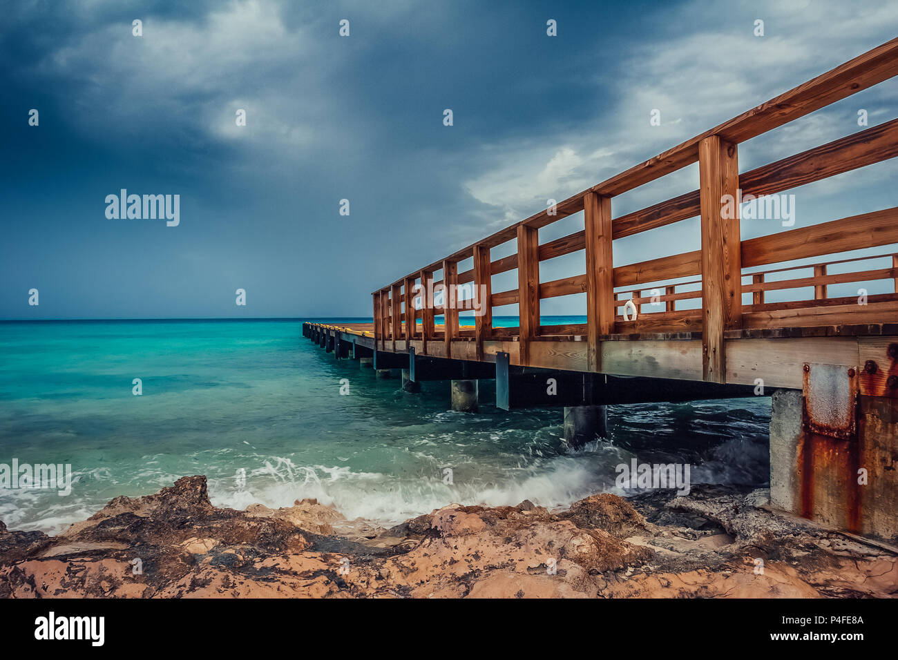 Blick auf die hölzerne Seebrücke von der türkisfarbenes Meer mit dramatischen Dunkelblaue Wolken. Stockfoto