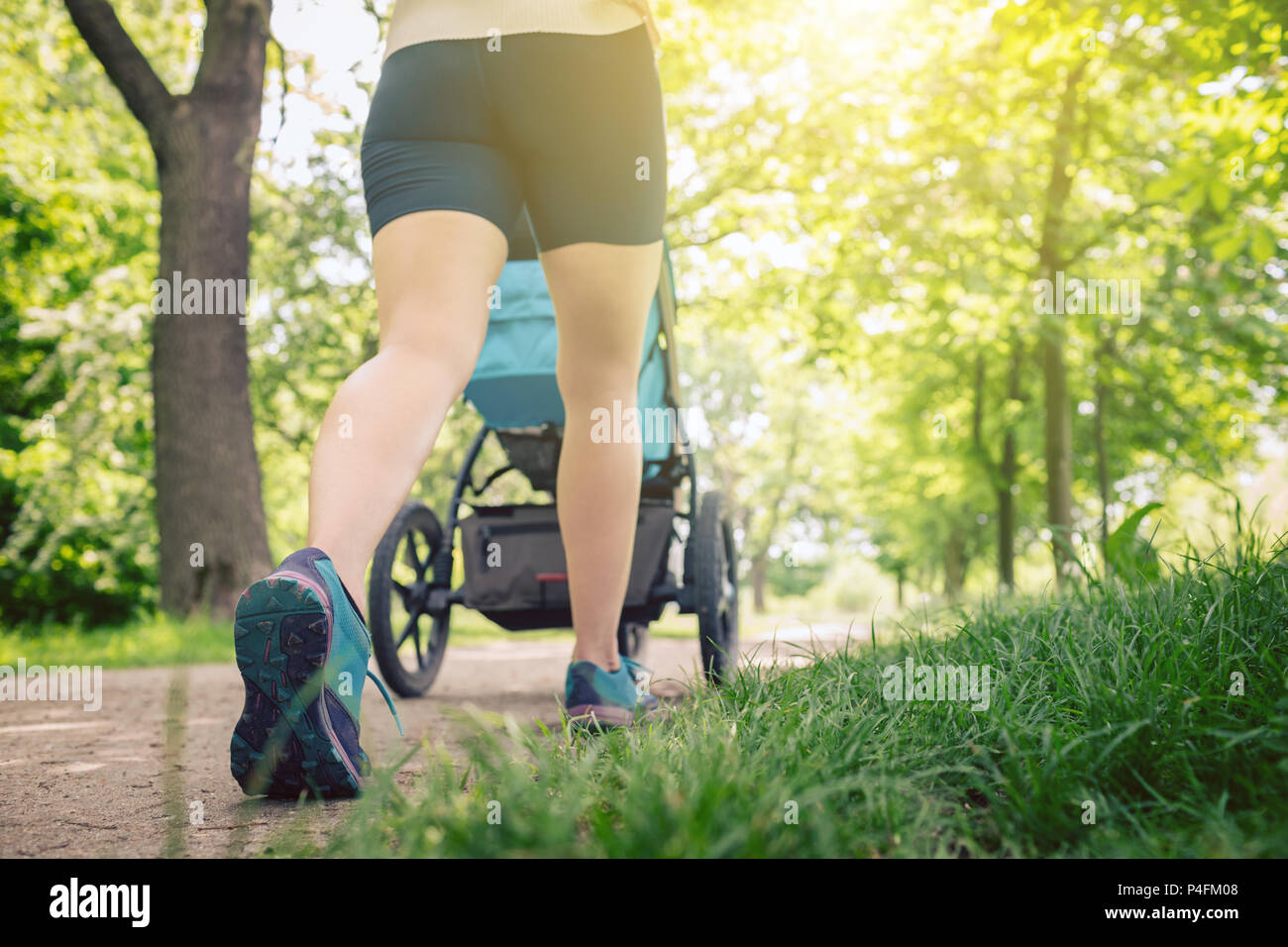 Walking Frau mit Kinderwagen geniessen Sommertag im Park. Joggen oder Walken supermom, aktive Familie mit Baby Jogger. Stockfoto