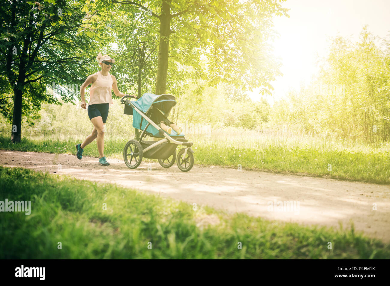 Läuft eine Frau mit Kinderwagen geniessen Sommertag im Park. Joggen oder Walken supermom, aktive Familie mit Baby Jogger. Stockfoto