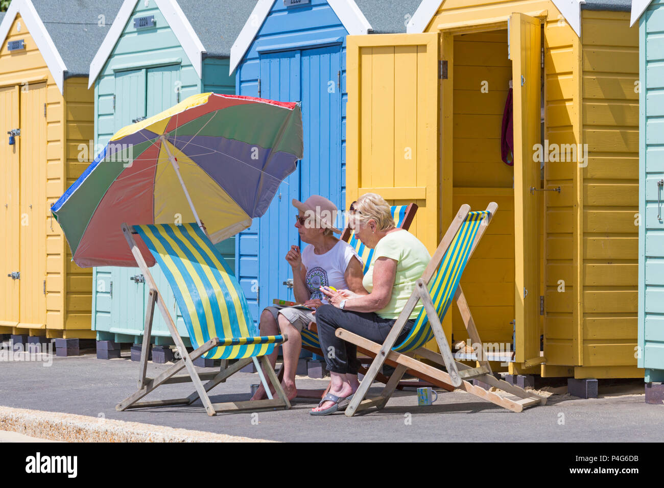 Bournemouth, Dorset, Großbritannien. Am 22. Juni 2018. UK Wetter: schön warmen sonnigen Tag in Bournemouth Strände als Besucher gehen zum Meer den Sonnenschein zu machen, wie die Prognose ist für Temperaturen weiter zu erhöhen. Zwei Frauen in Liegestühlen unter einem Sonnenschirm an der Promenade am Strand Hütten. Credit: Carolyn Jenkins/Alamy leben Nachrichten Stockfoto