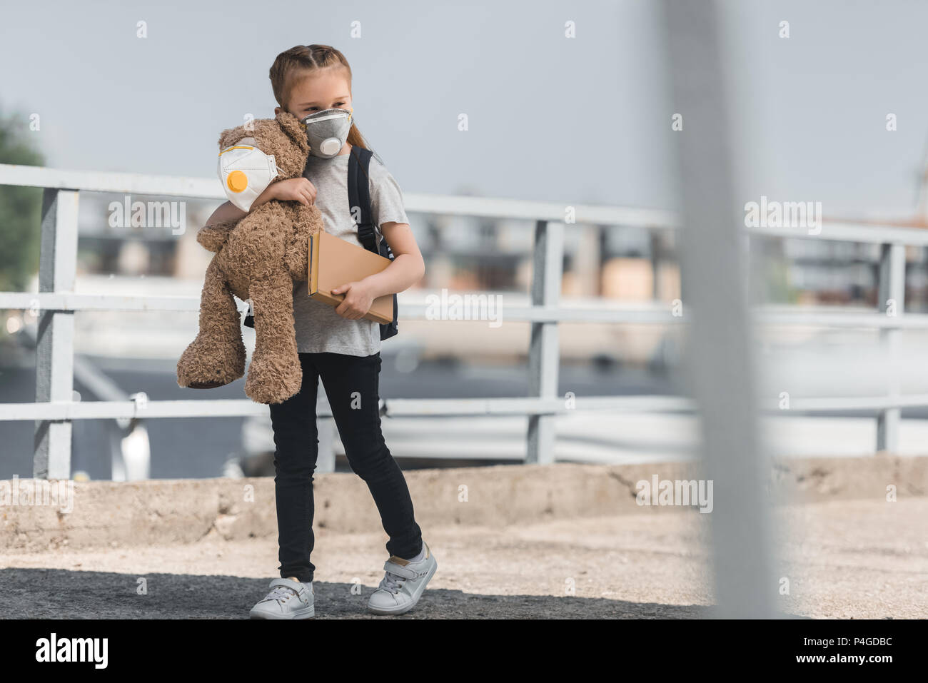 Kind in der Schutzmaske mit Teddy und Buch auf Brücke, Luftverschmutzung Konzept Stockfoto