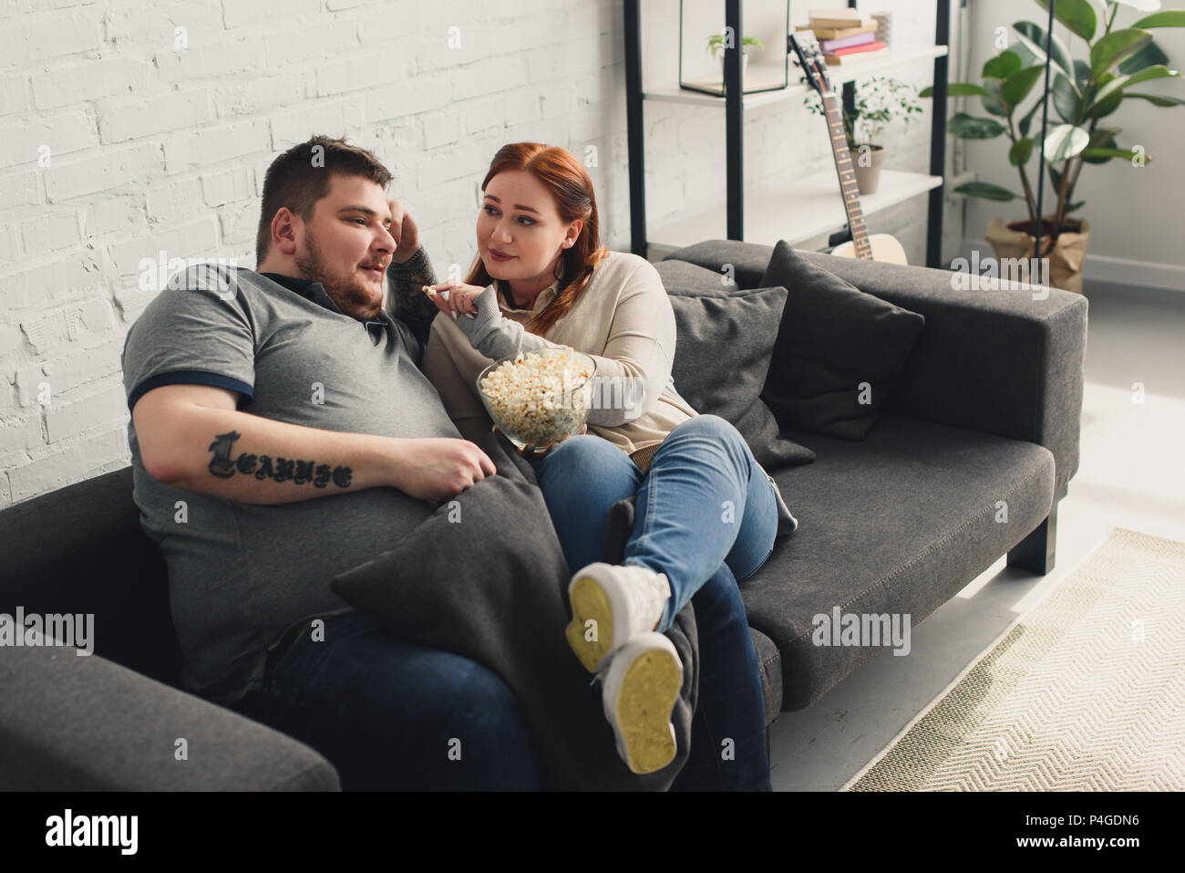 Größe plus Freundin Fütterung Freund mit Popcorn auf dem Sofa zu Hause Stockfoto