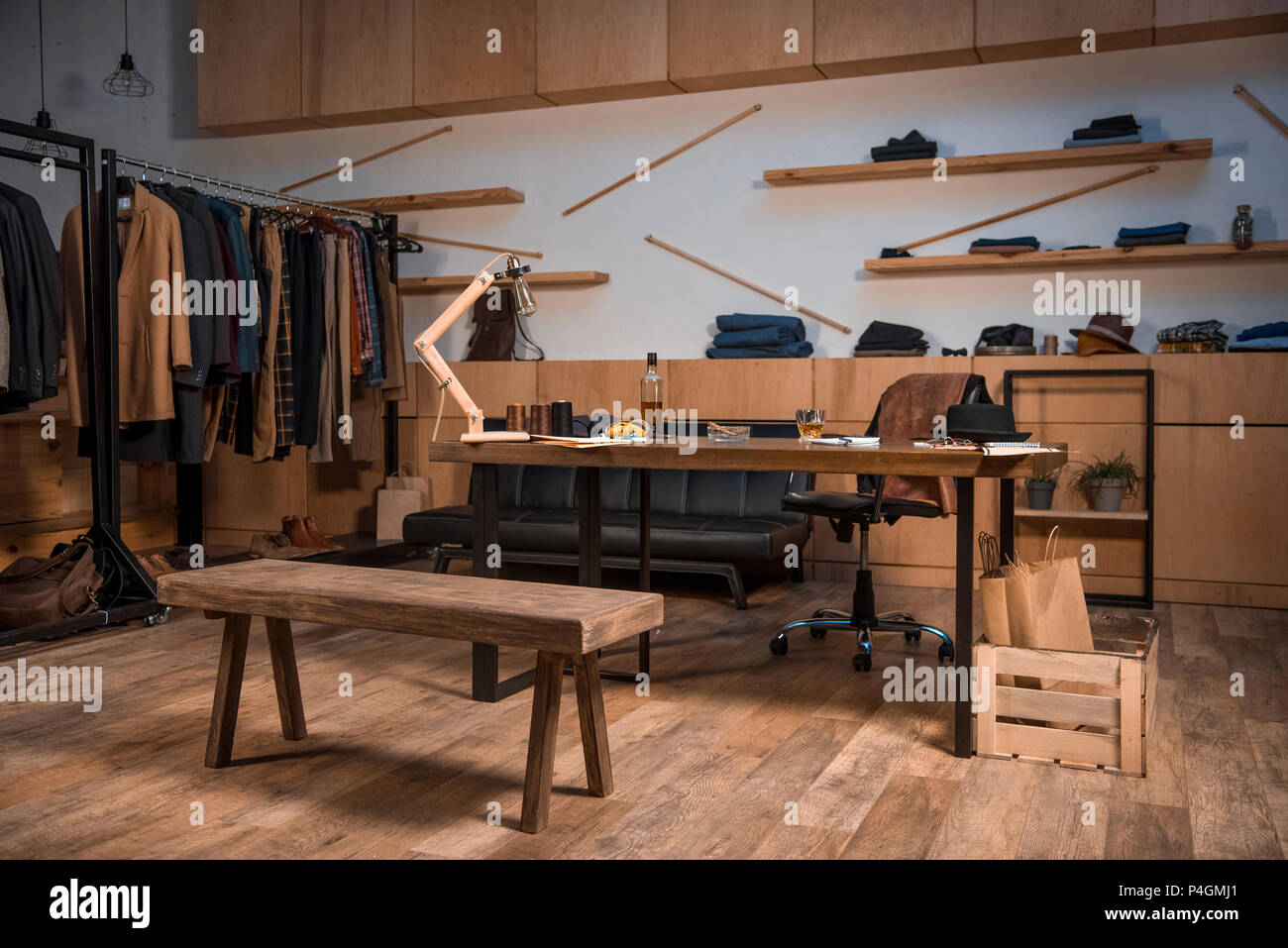Bekleidung Design Studio Interieur mit stilvoller Kleidung auf Kleiderbügeln und Flasche Whisky auf Tisch Stockfoto