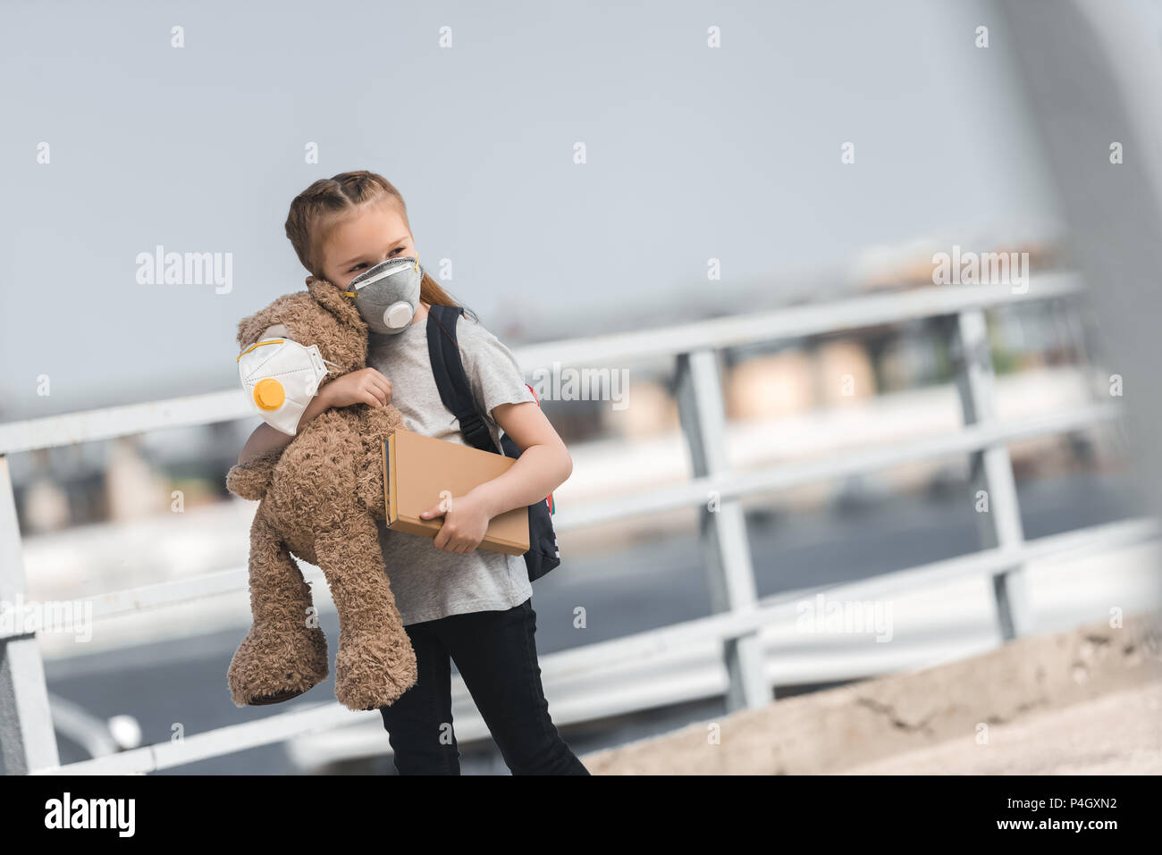 Kind in Schutzmaske mit Teddy und Buch auf Brücke, Luftverschmutzung Konzept Stockfoto