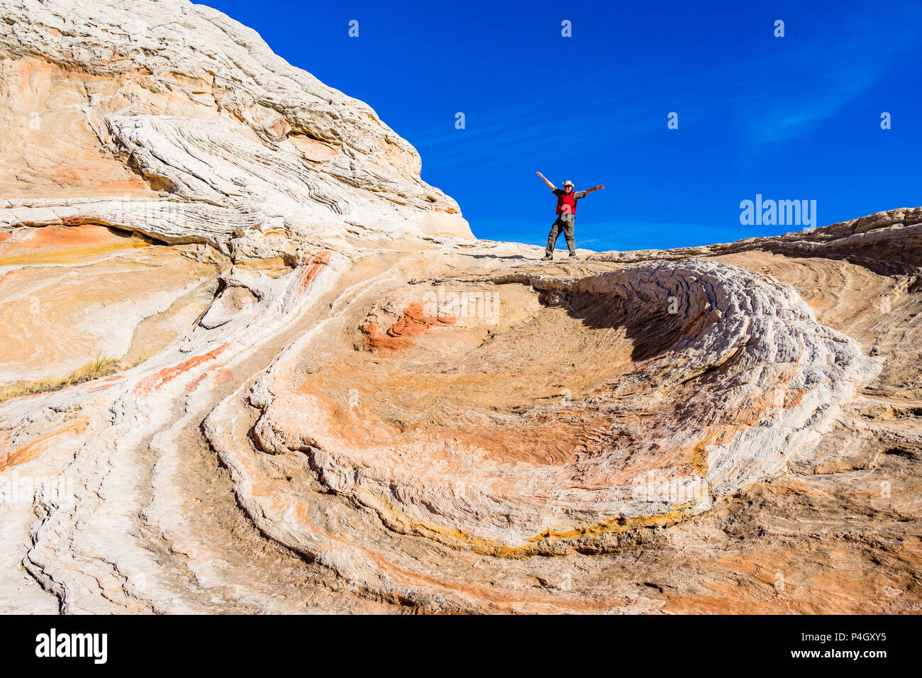 Mann, der gegen den blauen Himmel steht, mit ausgestreckten Armen über der Sandsteinvortex-Formation White Pocket Area Vermilion Cliffs National Monument, Arizona Stockfoto