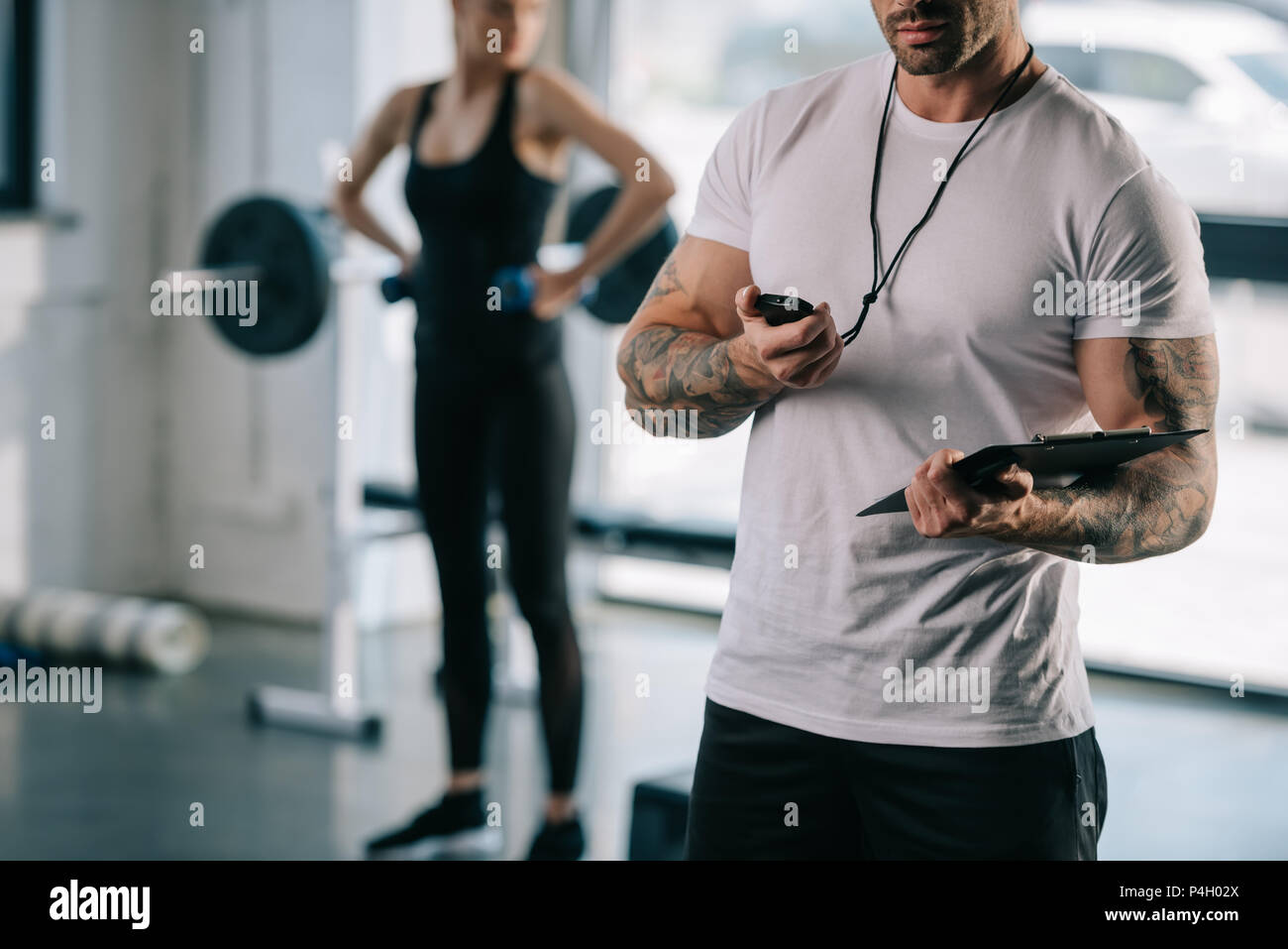 7/8 shot der männlichen Personal Trainer zu Timer und junge sportlerin Training mit Kurzhanteln hinter im Fitnessstudio suchen Stockfoto