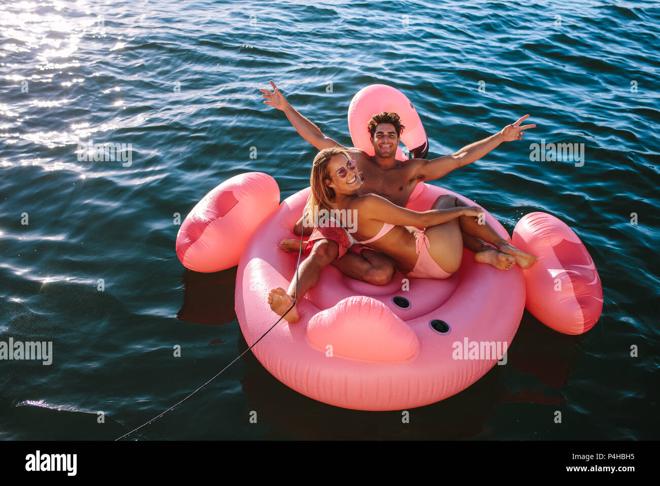 Attraktive Paar beim aufblasbaren Spielzeug Fahrt hinter einem Boot im Meer. Der Mann und die Frau sitzt auf einem aufblasbaren Spielzeug zu einem Boot im Meer gebunden. Stockfoto
