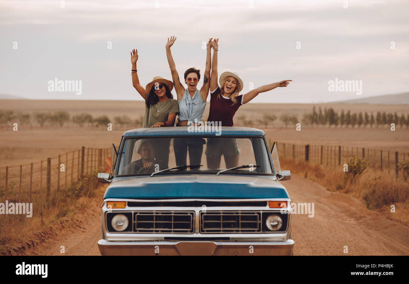 Gruppe von weiblichen Freunde Reiten in Pickup truck Spaß im Sommer Tag. Drei Frauen stehen an der Rückseite der Pickup Truck mit ihren Armen wirft und s Stockfoto