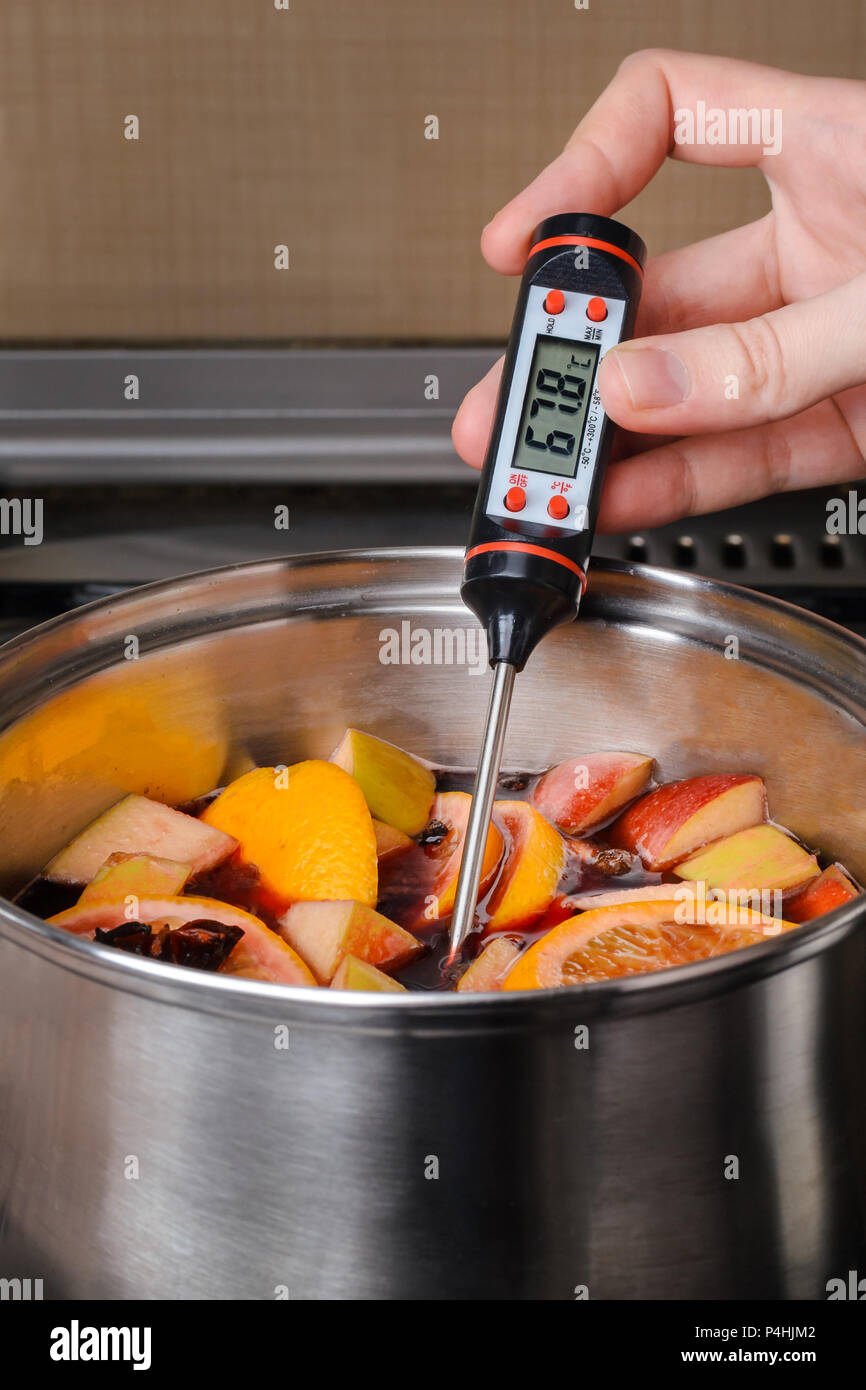 Der Prozess der Herstellung Glühwein in einem Topf, der Hand, misst die Temperatur der Glühwein mit ein elektronisches Thermometer Stockfotografie